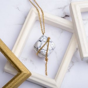 Com'une Alchimie vous présente le collier luxe Olympe en imitation marbre blanc et de forme cube une fine chaîne dorée en acier inoxydable de bijouterie vient parfaite cet élégant pendentif