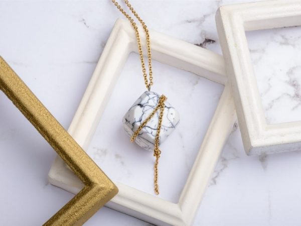 Com'une Alchimie vous présente le collier luxe Olympe en imitation marbre blanc et de forme cube une fine chaîne dorée en acier inoxydable de bijouterie vient parfaite cet élégant pendentif